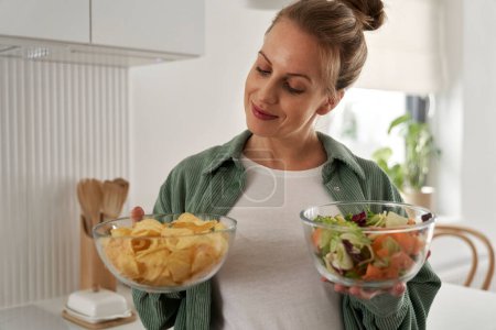 Téléchargez les photos : Femme enceinte au choix entre des chips et un bol de salade - en image libre de droit