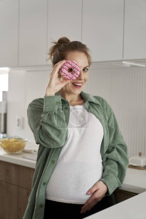 Téléchargez les photos : Femme enceinte s'amuser avec un beignet - en image libre de droit
