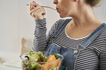 Téléchargez les photos : Femme caucasienne dans la cuisine manger un bol de salade - en image libre de droit