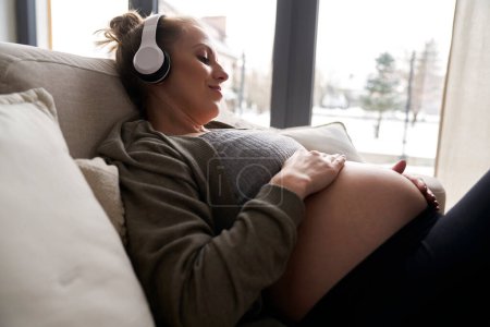 Téléchargez les photos : Femme enceinte caucasienne couchée sur le canapé et écoutant de la musique - en image libre de droit