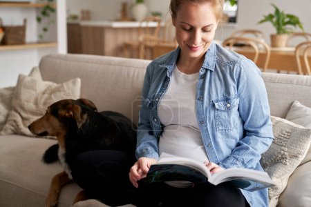 Photo for Caucasian pregnant woman sitting on sofa and reading a book - Royalty Free Image