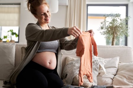 Téléchargez les photos : Femme enceinte pliant vêtements bébé - en image libre de droit