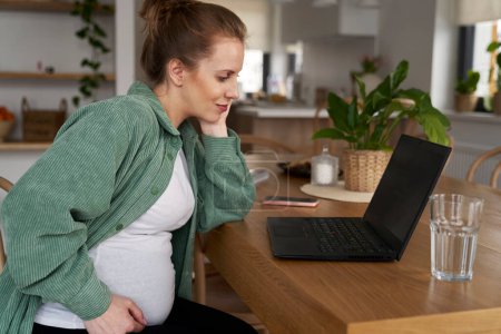 Foto de Mujer embarazada usando el ordenador portátil en casa - Imagen libre de derechos
