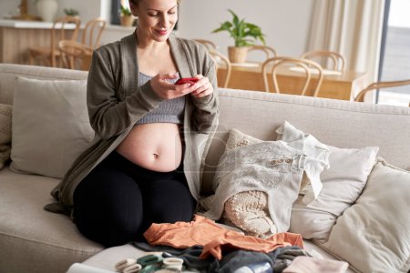 Téléchargez les photos : Femme enceinte prenant des photos de vêtements de bébé - en image libre de droit