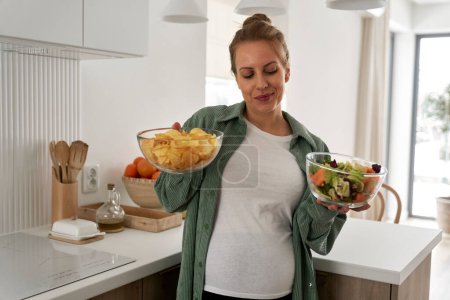 Photo for Pregnant woman choosing between crisps and a bowl of salad - Royalty Free Image