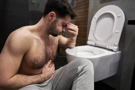 Foto de Hombre enfermo con dolor de estómago al lado del inodoro - Imagen libre de derechos
