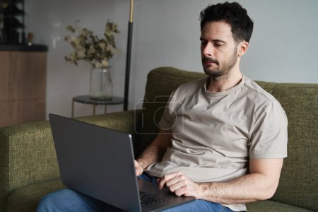 Téléchargez les photos : Homme travaillant sur ordinateur portable sur canapé - en image libre de droit