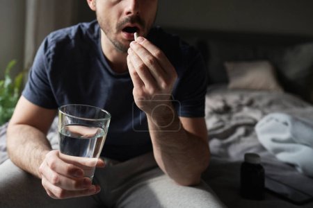 Man sitting on bed and taking pills