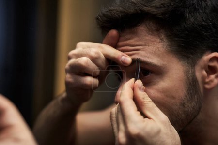 Téléchargez les photos : Jeune homme arrachant les sourcils dans la salle de bain domestique - en image libre de droit