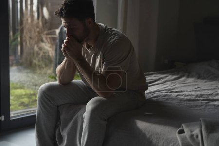 Téléchargez les photos : Homme anxieux à la maison assis sur le lit et regardant loin - en image libre de droit