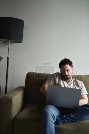 Téléchargez les photos : Homme utilisant un ordinateur portable et appelant assis sur le canapé - en image libre de droit