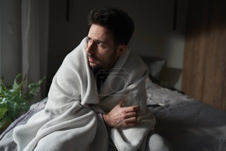 Foto de Hombre enfermo bebiendo medicina en vidrio mientras está sentado debajo de la manta - Imagen libre de derechos
