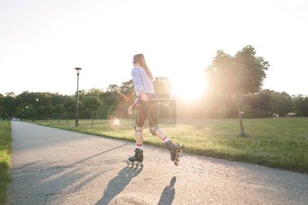 Téléchargez les photos : Vue arrière de la jeune femme faisant du roller dans le parc - en image libre de droit