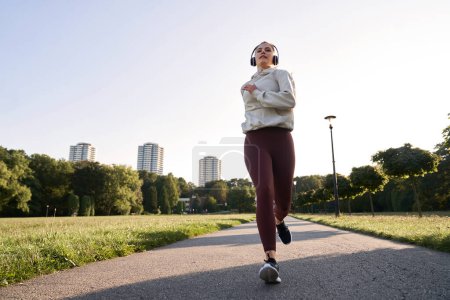Téléchargez les photos : Plan large de la femme faisant du jogging dans le parc pendant le coucher du soleil - en image libre de droit