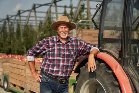 Téléchargez les photos : Portrait d'un agriculteur âgé à côté d'un tracteur - en image libre de droit