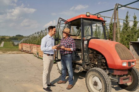 Téléchargez les photos : Agriculteur senior et représentant des ventes parler sur tablette numérique sur verger de pommes - en image libre de droit