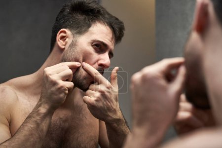 Téléchargez les photos : Homme caucasien vérifier l'état du visage dans la salle de bain - en image libre de droit