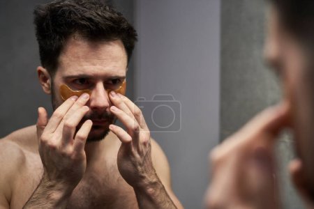 Téléchargez les photos : Homme caucasien appliquant patch cosmétique sous les yeux - en image libre de droit