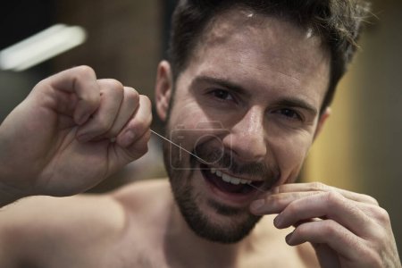Téléchargez les photos : Homme utilisant de la soie dentaire dans la salle de bain domestique - en image libre de droit