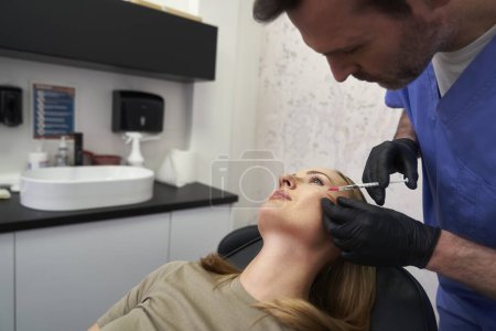 Foto de Mujer que se somete a un procedimiento de lifting facial realizado por un médico varón - Imagen libre de derechos