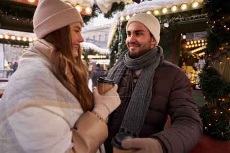 Téléchargez les photos : Couple caucasien boire du vin chaud et bavarder sur le marché de Noël - en image libre de droit