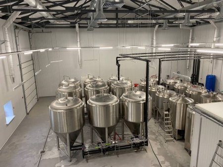 Foto de Grandes cubas metálicas en las que se fermenta vino o cerveza en la fábrica de la bodega. Concepto de tecnologías y equipos para la producción de bebidas alcohólicas - Imagen libre de derechos