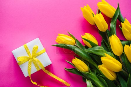 Téléchargez les photos : Bouquet of yellow tulips with gift box on pink background. Space for message. Flowers concept. Spring. Holiday greeting card for Valentine's, Women's, Mother's Day, Easter. Birthday. Top view. - en image libre de droit