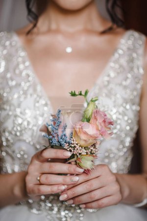 Téléchargez les photos : La mariée tenant à la main le gros plan des fleurs de boutonnière du marié avec des roses et du vert et de la verdure. Les préparatifs de la mariée. Mariage Concept du matin. - en image libre de droit