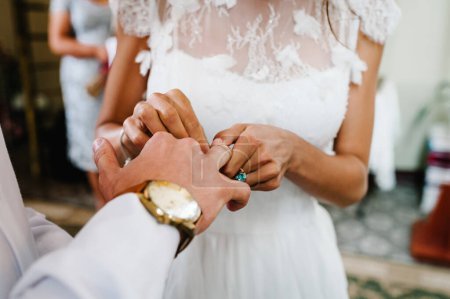 Foto de La mano de la novia lleva un anillo de oro de compromiso en el dedo del novio. Día de la boda. Manos con anillos de boda. De cerca.. - Imagen libre de derechos