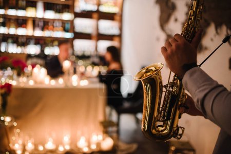 Téléchargez les photos : Les mains du saxophoniste en jouant du jazz. Musicien tenir saxophone à date romantique le jour de la Saint-Valentin au restaurant. Homme jouant du saxophone à la fête ou au mariage. Concept de musique jazz en gros plan. Espace pour le texte - en image libre de droit