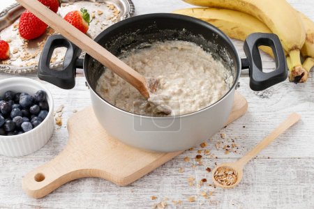 Téléchargez les photos : Une casserole de porridge parmi les fruits frais. Une nourriture saine. Temps de cuisson - en image libre de droit