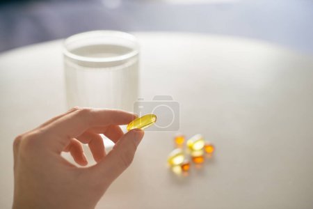 Photo for Close up of woman hand taking yellow capsule of omega 3, 6, 9 vitamins and D . Winter health care concept. Selective focus natural light photo. - Royalty Free Image