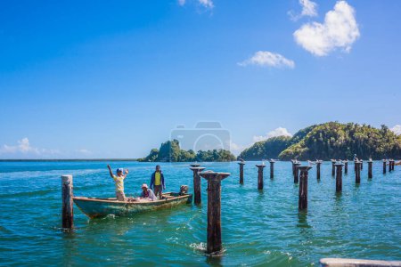 Photo for Dominican Republic. 20 NOVEMBER 2021 Fishermen on a small old boat. Seagulls on the top of the pier support pylons. Seagulls on pier supports. Sunny warm day at the sea under palm trees. Sun loungers under palm trees - Royalty Free Image