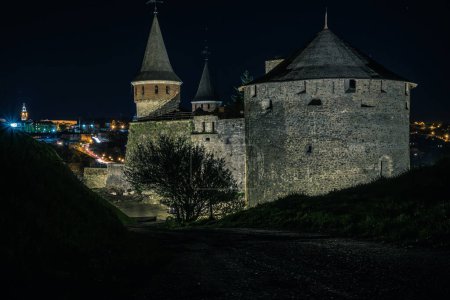 Téléchargez les photos : Vue sur le château de Kamianets-Podilskyi en soirée. Beau château en pierre sur la colline au coucher du soleil. Nuages dans le ciel sombre au-dessus du château. L'heure bleue. Ukraine - en image libre de droit