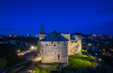 Téléchargez les photos : Vue sur le château de Kamianets-Podilskyi en soirée. Beau château en pierre sur la colline au coucher du soleil. Nuages dans le ciel sombre au-dessus du château. L'heure bleue. Ukraine - en image libre de droit