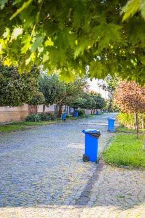 Blaue Mülltonnen auf der Straße in einer kleinen Stadt in der Nähe jedes Hauses. Zentrale Müllabfuhr in einer kleinen, gemütlichen europäischen Stadt. Müllabfuhr an einem bestimmten Wochentag.