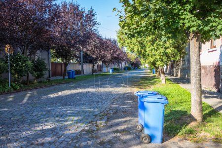 Latas de basura azul en la calle en un pequeño pueblo cerca de cada casa. Recogida centralizada de basura en una pequeña y acogedora ciudad europea. Recogida de basura en un cierto día de la semana.