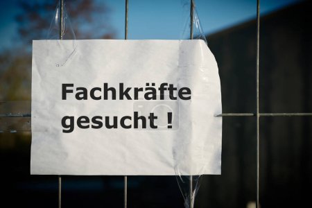  Notice on the fence of a company in Germany with the inscription Fachkrafte gesucht. Translation of the text: Professionals wanted                                