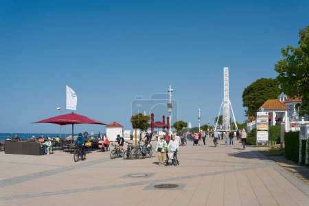 Photo for Kuehlungsborn, Germany  May 27, 2023: Holidaymakers on the beach promenade of the popular resort Kuehlungsborn with cafe and Ferris wheel on the Baltic Sea - Royalty Free Image