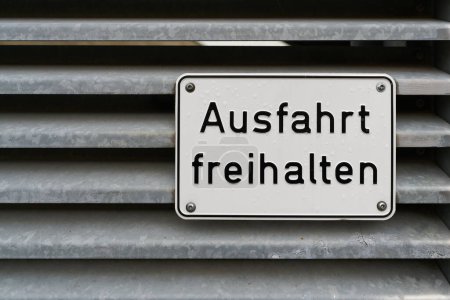 Schild am Tor eines Parkhauses mit der deutschen Aufschrift Ausfahrt freihalten. Übersetzung: Keep exit clear                               