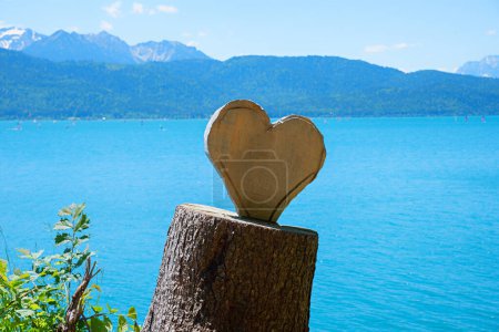Photo for Tree trunk with wooden carved heart, mountains background. beautiful love symbol at the lake shore walchensee - Royalty Free Image