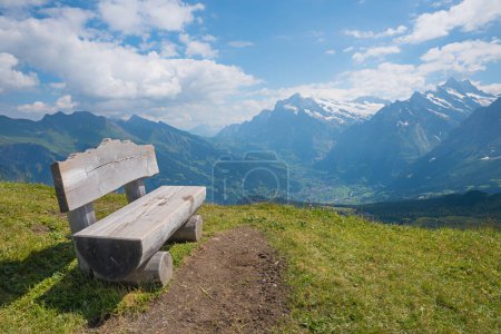 wooden bench at Mannlichen mountain, view to Grindelwald tourist resort swiss alps. blue sky with clouds