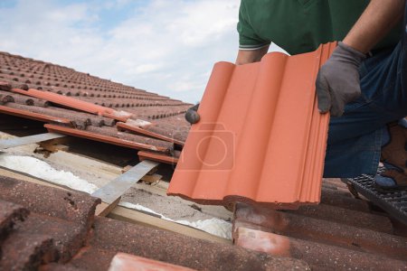 Photo for Man fit in new roof shingels on the house rooftop, replacing the old and damaged ones - Royalty Free Image