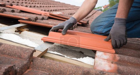 Photo for Man fit in new roof shingels on the house rooftop, replacing the old and damaged ones - Royalty Free Image