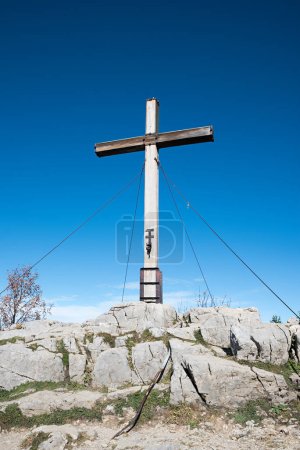 Bergkreuz Kampenwand, auf felsigem Boden stehend, blauer Himmelshintergrund