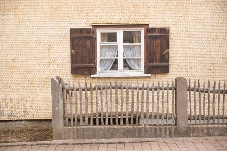 fachada de la casa con tejas de madera a escala de pescado y ventana de celosía con persianas marrones. cerca de madera.