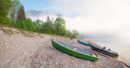 Nebel über dem Sylvensteinsee, Kiesstrand mit Booten, grüne Frühlingslandschaft Oberbayern