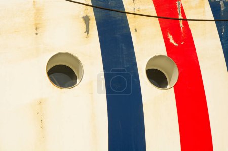 Zwei Bullaugen im Schiffsrumpf mit weißen, blauen und roten Streifen