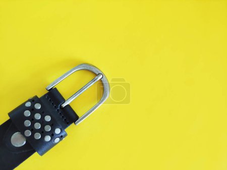 Cinturón negro de cuero para mujer con hebilla de metal sobre fondo amarillo