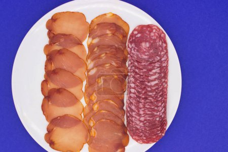 Sliced salami delicately arranged on a white plate over blue